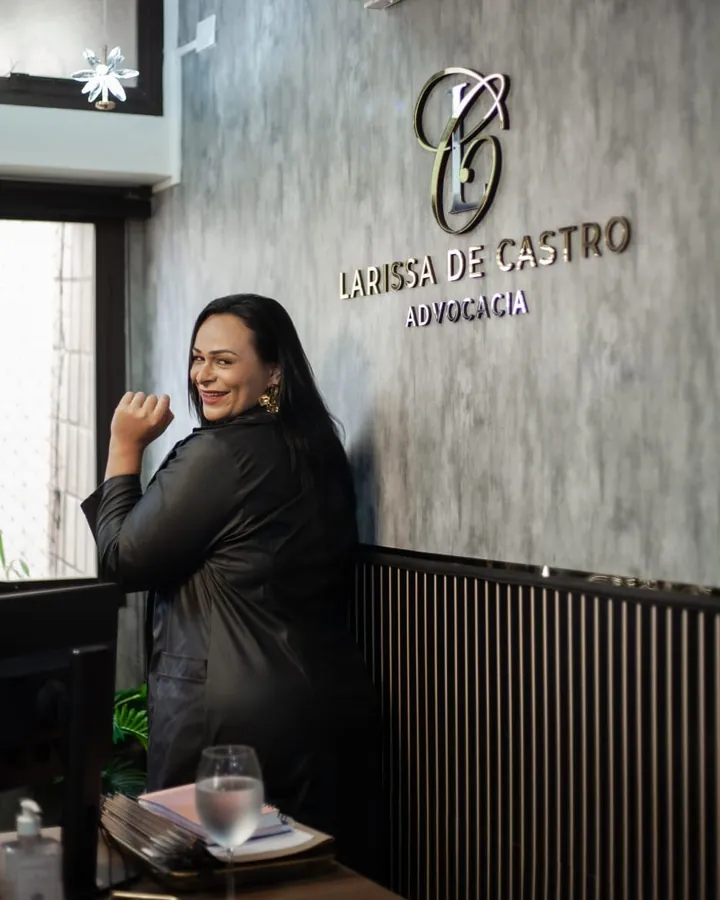 Dra. Larissa de Castro sorrindo em frente ao logotipo do escritório
